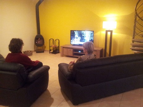 Two persons are sitting in front of the fire and television in the community room